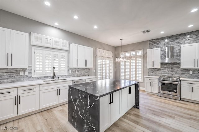 kitchen with a sink, wall chimney exhaust hood, white cabinets, and stainless steel range