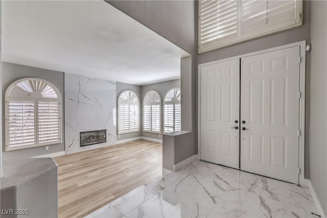 entryway featuring an accent wall, a fireplace, marble finish floor, and baseboards