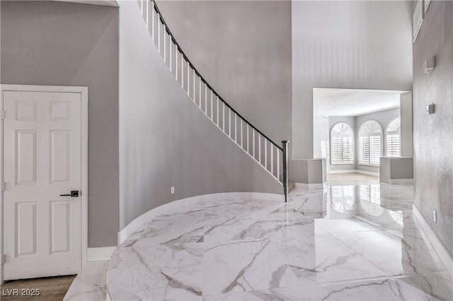 stairs with marble finish floor, baseboards, and a towering ceiling