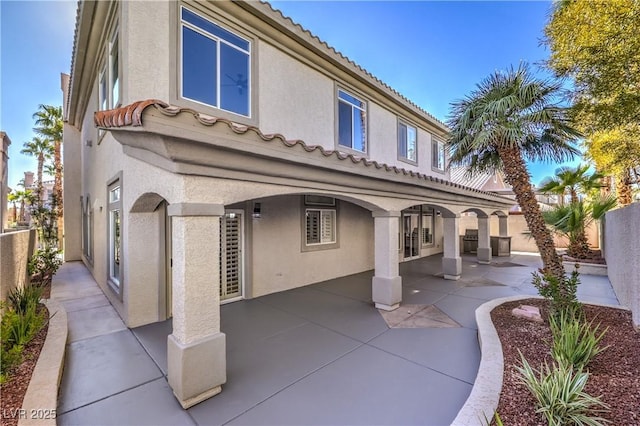 rear view of house with stucco siding, a tile roof, a patio, and fence