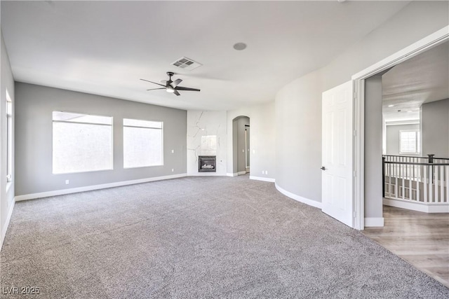 unfurnished living room with arched walkways, visible vents, a fireplace, and baseboards