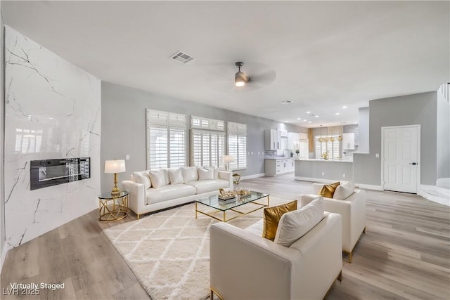 8864 La Manga Ave, Las Vegas, NV 89147 - living room featuring light wood finished floors, baseboards, visible vents, a ceiling fan, and a high end fireplace