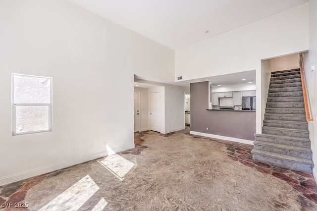 unfurnished living room featuring stairway, baseboards, and a towering ceiling