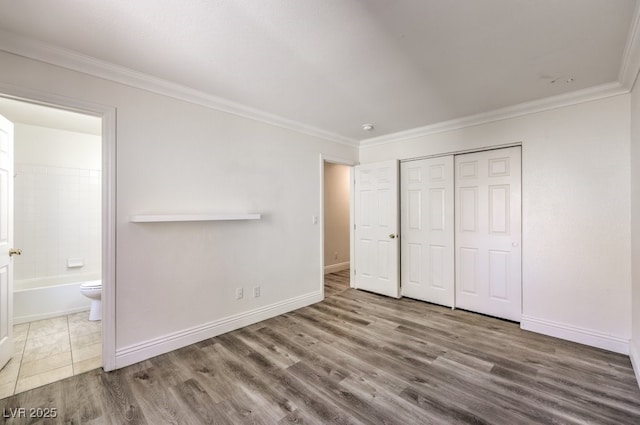 unfurnished bedroom featuring wood finished floors, baseboards, ensuite bathroom, and ornamental molding