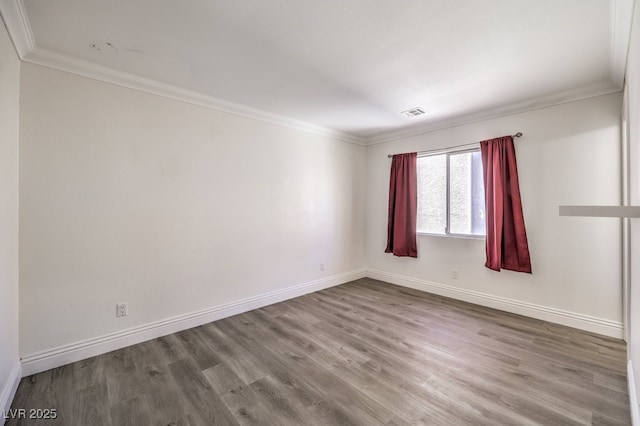 spare room featuring visible vents, wood finished floors, baseboards, and ornamental molding