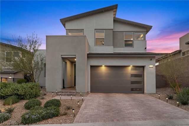 contemporary home featuring stucco siding, an attached garage, decorative driveway, and fence