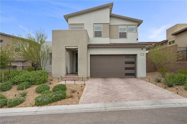 contemporary house with decorative driveway, fence, a garage, and stucco siding