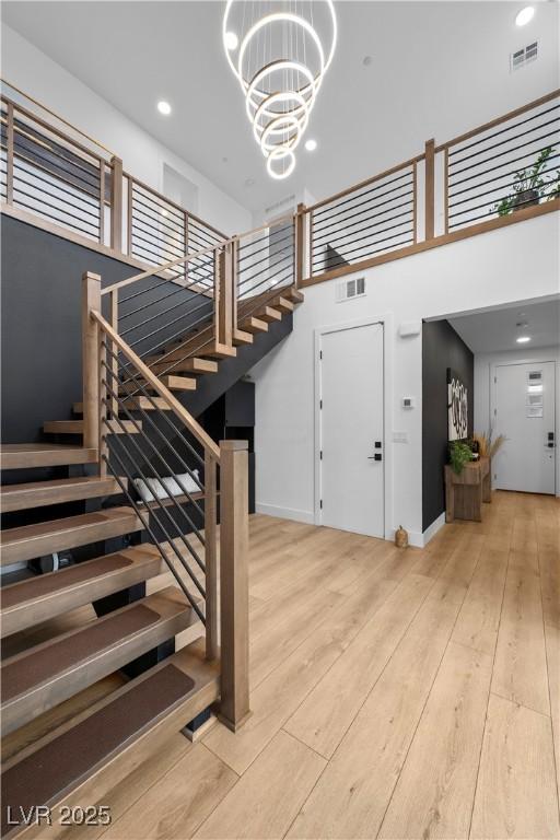 staircase with a notable chandelier, wood finished floors, visible vents, and baseboards