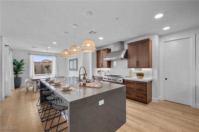 kitchen featuring visible vents, a breakfast bar, a center island with sink, light wood-style floors, and wall chimney exhaust hood