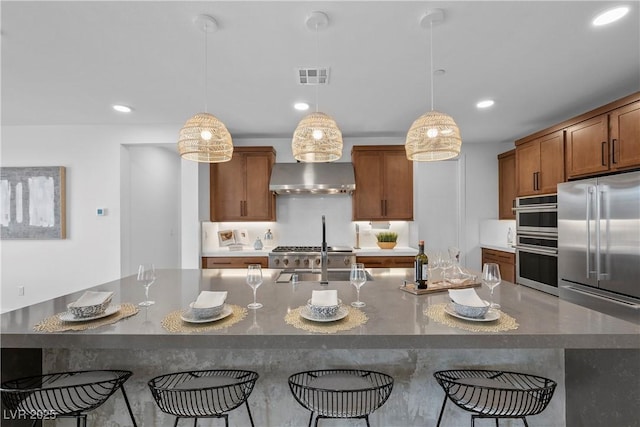 kitchen featuring visible vents, pendant lighting, range hood, appliances with stainless steel finishes, and a breakfast bar area