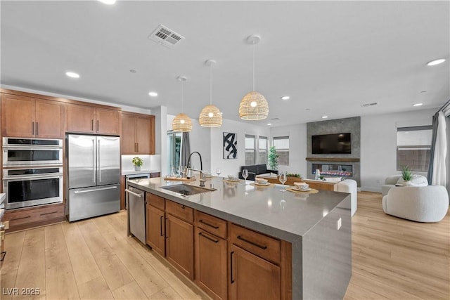 kitchen featuring light wood finished floors, visible vents, a large fireplace, stainless steel appliances, and a sink