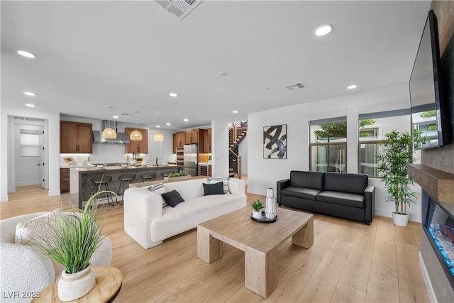 living room featuring recessed lighting, visible vents, light wood-style floors, and stairway