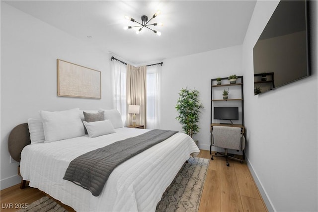 bedroom featuring an inviting chandelier, baseboards, and light wood-style floors