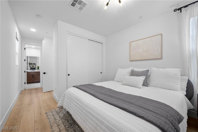 bedroom with light wood-type flooring, visible vents, ensuite bath, a closet, and baseboards