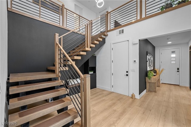 stairway with wood finished floors, visible vents, a towering ceiling, and baseboards