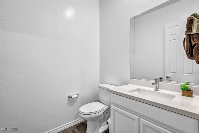 half bathroom featuring baseboards, toilet, and vanity