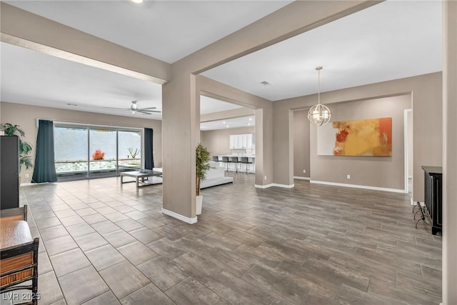 unfurnished living room featuring ceiling fan with notable chandelier and baseboards