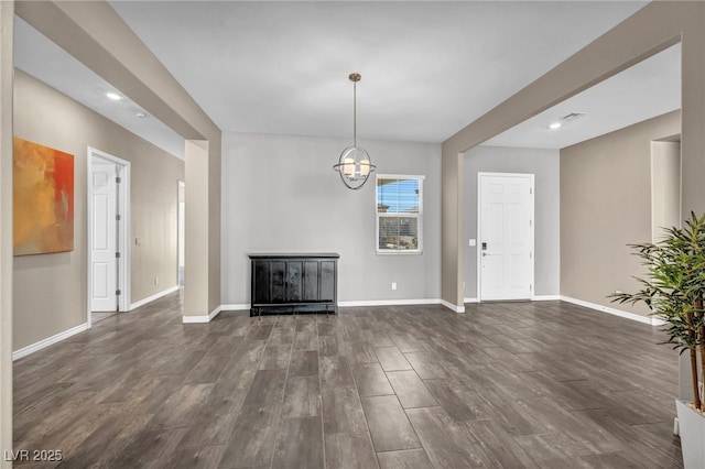 unfurnished living room featuring a notable chandelier, baseboards, and dark wood-style flooring