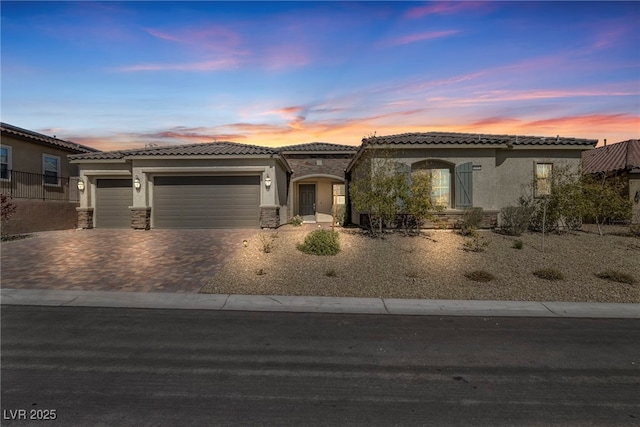 view of front facade with stucco siding, decorative driveway, stone siding, an attached garage, and a tiled roof