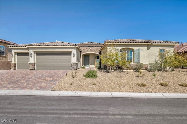 mediterranean / spanish home featuring stucco siding, a garage, stone siding, a tiled roof, and decorative driveway