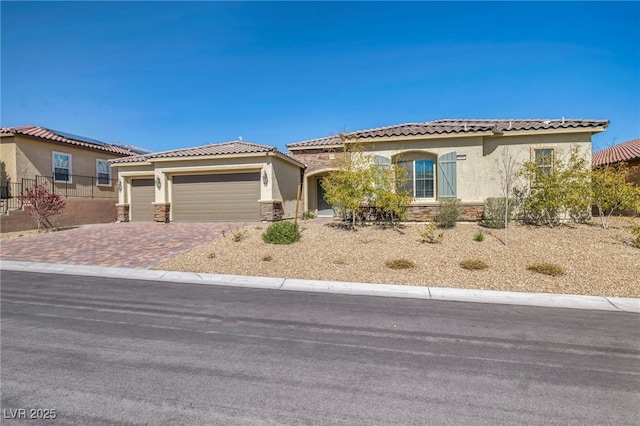 mediterranean / spanish house featuring decorative driveway, stone siding, an attached garage, and stucco siding