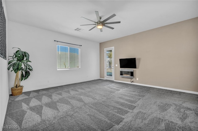 unfurnished living room with a glass covered fireplace, carpet, visible vents, and a wealth of natural light