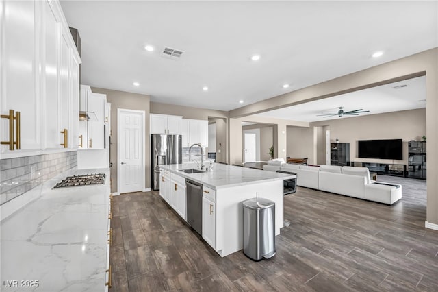 kitchen with light stone countertops, decorative backsplash, white cabinets, stainless steel appliances, and a sink