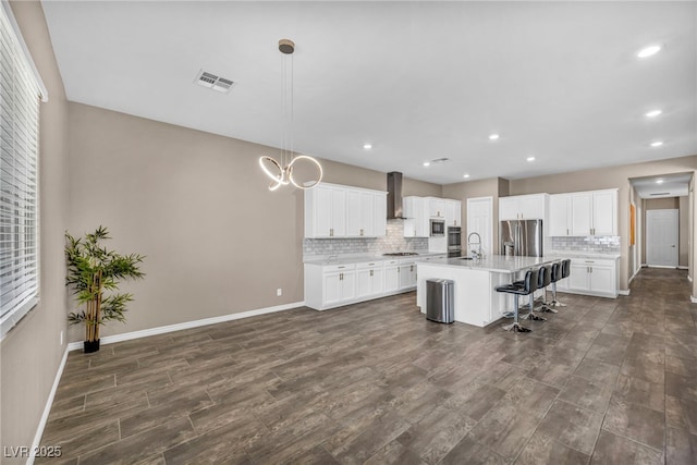 kitchen featuring visible vents, stainless steel appliances, light countertops, wall chimney exhaust hood, and backsplash