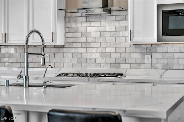 kitchen featuring light stone counters, a sink, white cabinets, black microwave, and tasteful backsplash