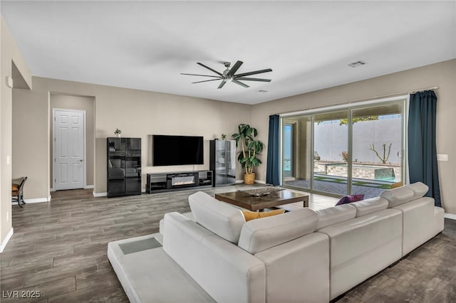 living area with visible vents, a glass covered fireplace, baseboards, ceiling fan, and wood tiled floor