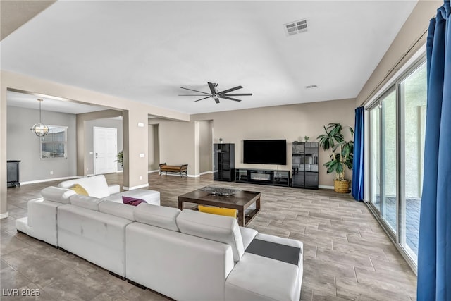 living room featuring visible vents, ceiling fan with notable chandelier, and baseboards