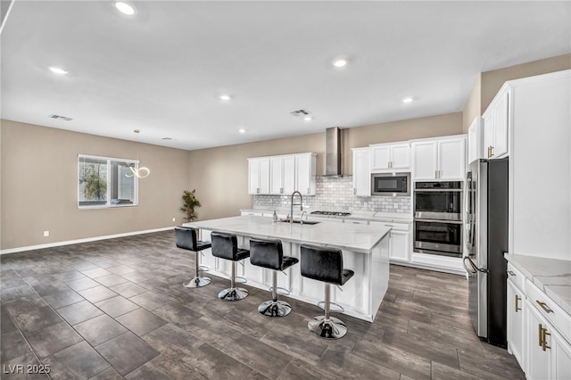 kitchen featuring a sink, stainless steel appliances, a kitchen bar, wall chimney exhaust hood, and tasteful backsplash