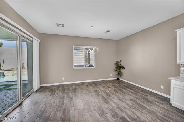 spare room with visible vents, baseboards, a notable chandelier, and dark wood finished floors