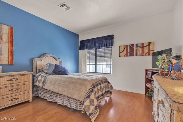 bedroom with wood finished floors, visible vents, and baseboards