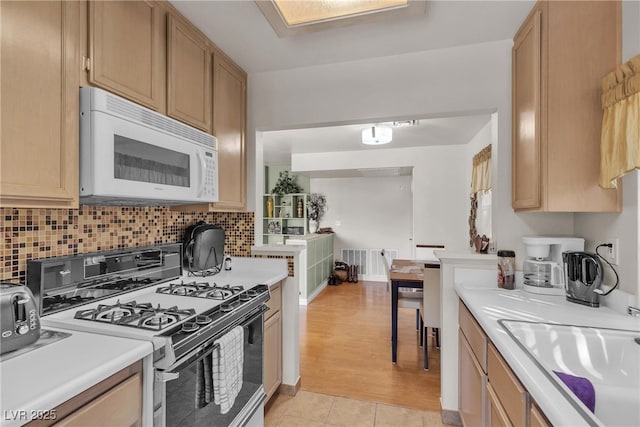 kitchen featuring white microwave, tasteful backsplash, gas range, light countertops, and a sink