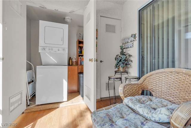 clothes washing area featuring visible vents, stacked washer and clothes dryer, laundry area, and wood finished floors