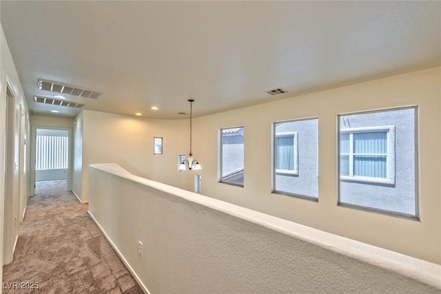 hall with a notable chandelier, carpet flooring, baseboards, and visible vents