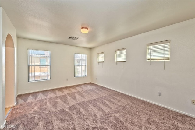 spare room with visible vents, arched walkways, carpet, and baseboards