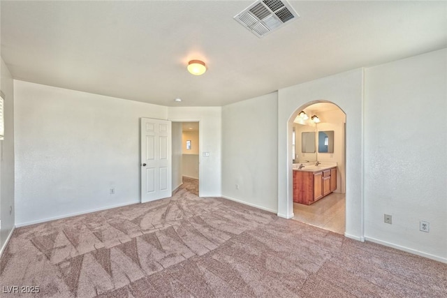 unfurnished bedroom featuring arched walkways, visible vents, light carpet, and baseboards