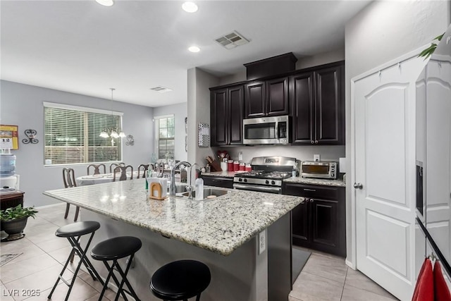 kitchen with visible vents, light tile patterned floors, appliances with stainless steel finishes, a kitchen breakfast bar, and a sink