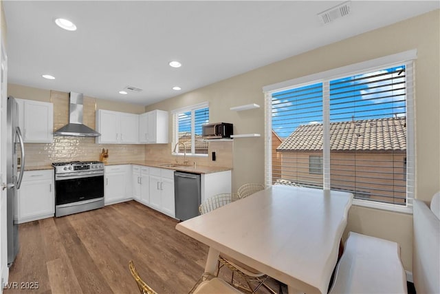 kitchen featuring wood finished floors, a sink, appliances with stainless steel finishes, wall chimney exhaust hood, and backsplash