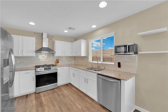 kitchen with light wood finished floors, visible vents, wall chimney range hood, stainless steel appliances, and a sink