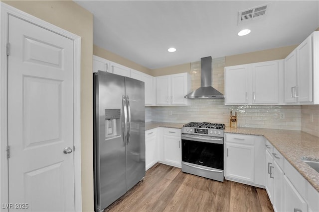 kitchen featuring visible vents, light stone counters, white cabinetry, stainless steel appliances, and wall chimney range hood