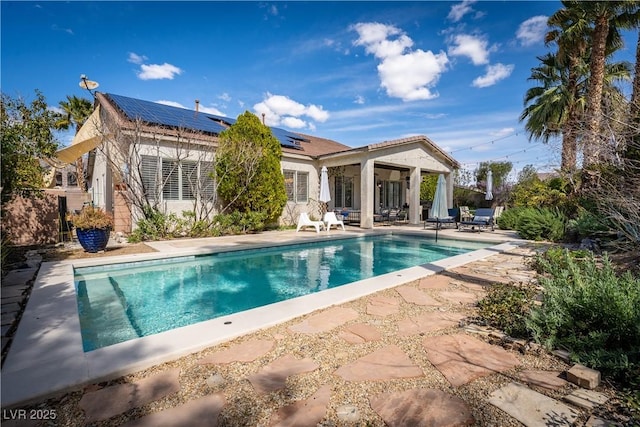 rear view of property with a patio area, an outdoor pool, and roof mounted solar panels