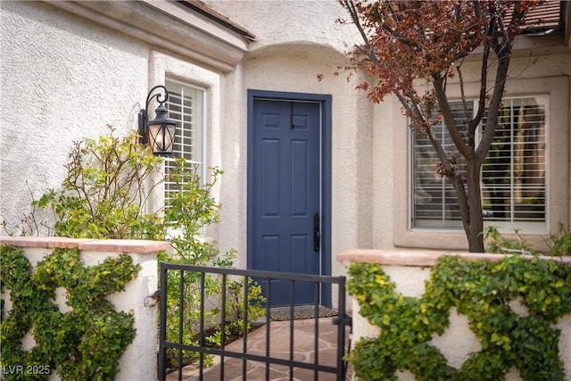 view of exterior entry featuring stucco siding and a gate