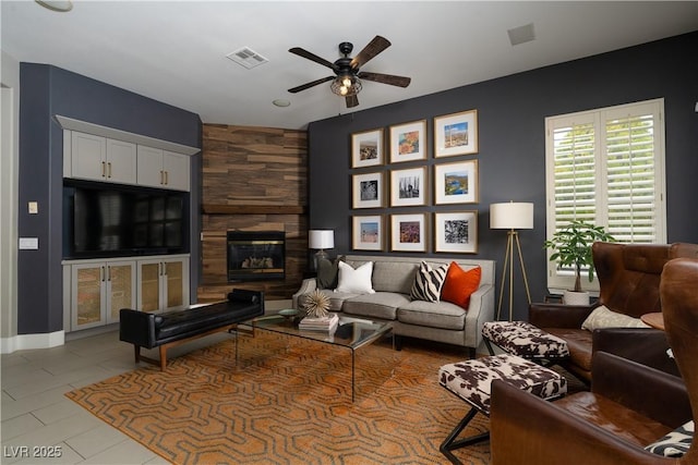 living area with tile patterned flooring, visible vents, a large fireplace, baseboards, and a ceiling fan