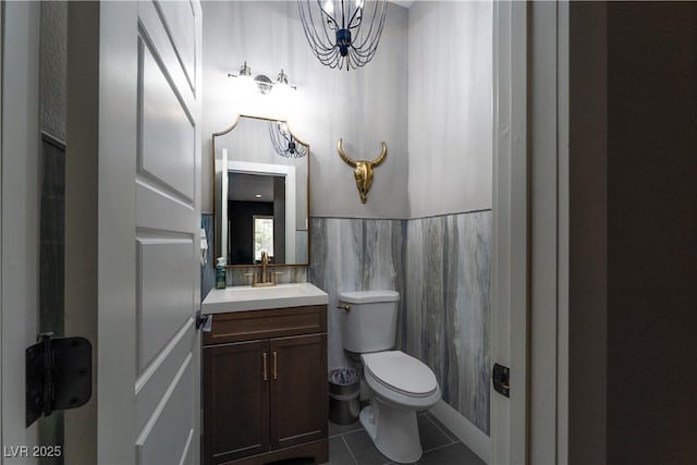 bathroom with tile patterned flooring, toilet, vanity, a notable chandelier, and tile walls