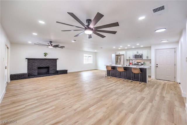 living area featuring light wood-style flooring, a fireplace, visible vents, and ceiling fan