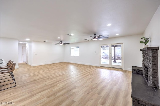 living room with visible vents, a ceiling fan, a fireplace, light wood finished floors, and baseboards