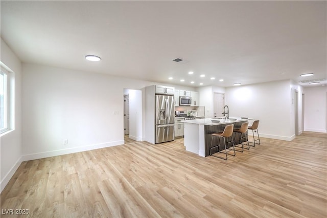 kitchen featuring a breakfast bar, baseboards, stainless steel appliances, and light wood-style floors